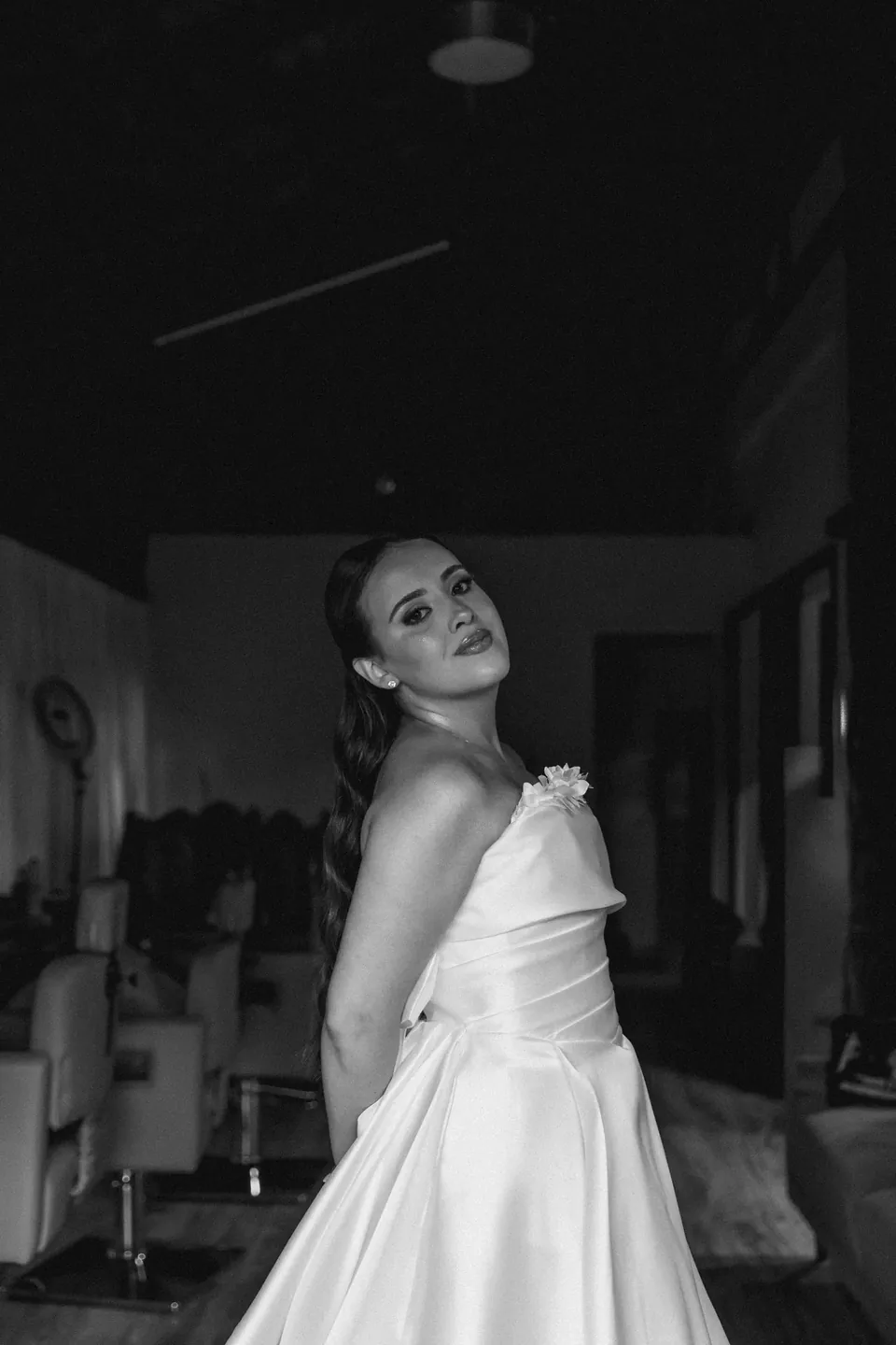 Retrato em preto e branco da noiva já vestida no camarim, com as poltronas de beleza ao fundo
